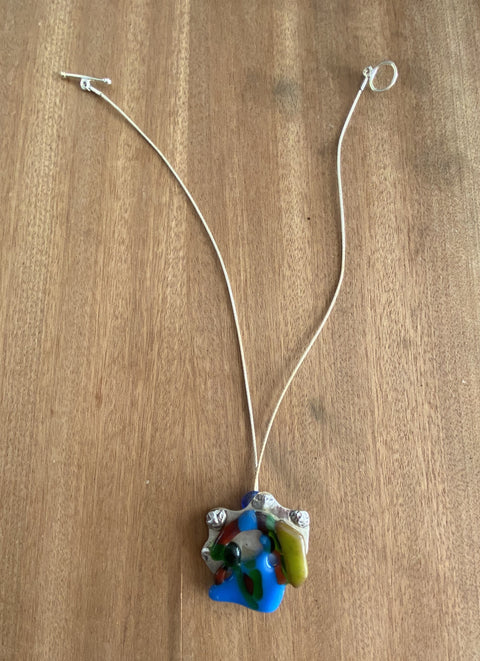 Een zilveren ketting met handgemaakte hanger van zilver met gefused glas